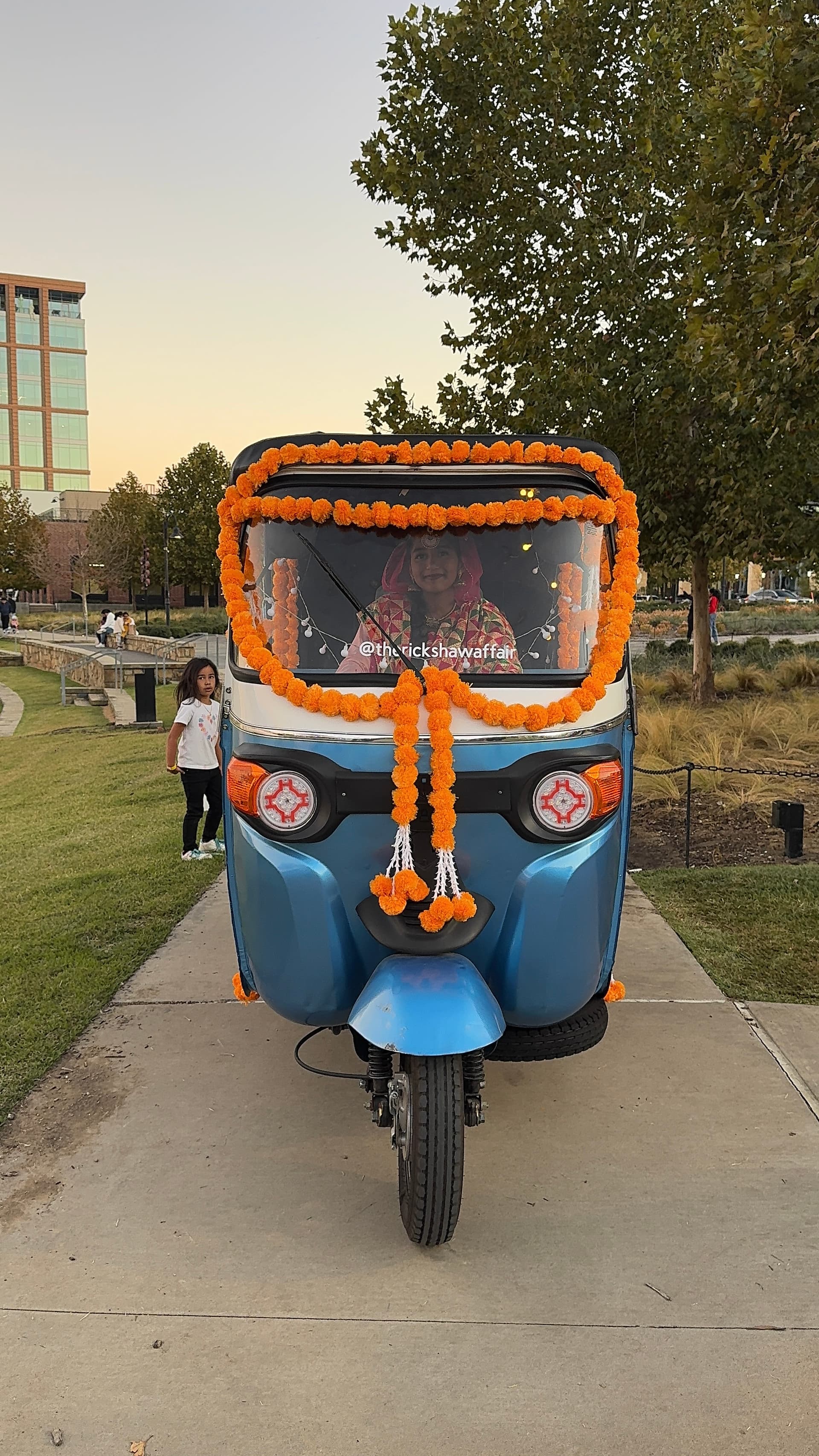 The rickshaw dressed in orange marigold garlands and signage at a Dallas-Fort Worth event