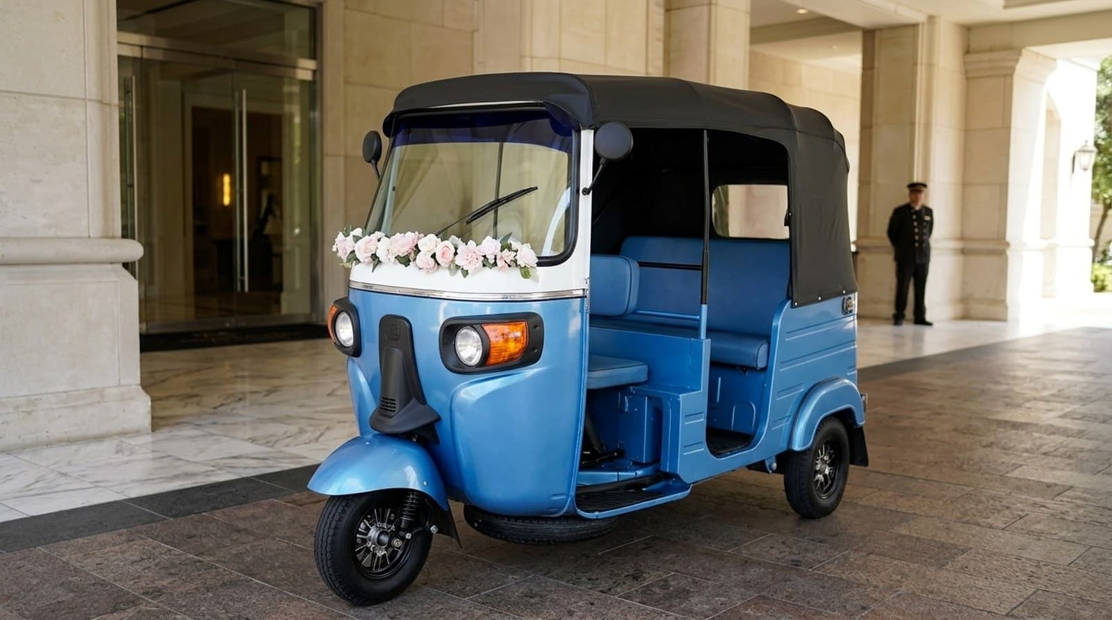 The blue and white electric rickshaw with a floral garland parked at a hotel entrance.