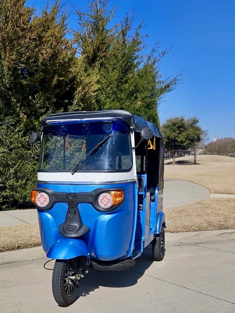The 2024 blue and white electric rickshaw parked on a driveway, undecorated